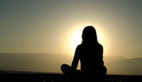 a silhouette of a woman sitting on the beach at sunset